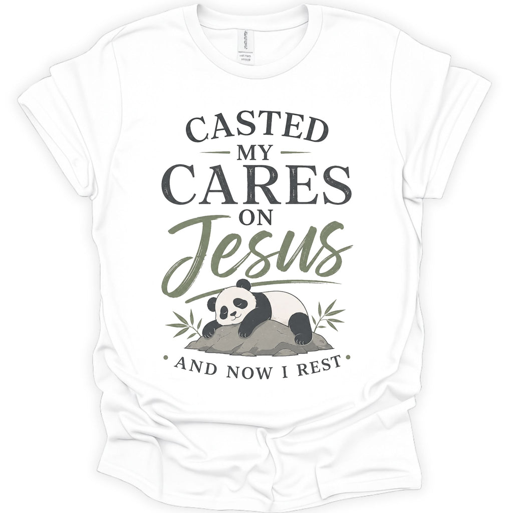 A white short-sleeve crewneck t-shirt with a graphic print on the front. The print features the text 'CASTED MY CARES ON Jesus AND NOW I REST' in dark gray and olive green lettering, accompanied by an illustration of a sleeping panda resting on a rock with bamboo leaves.