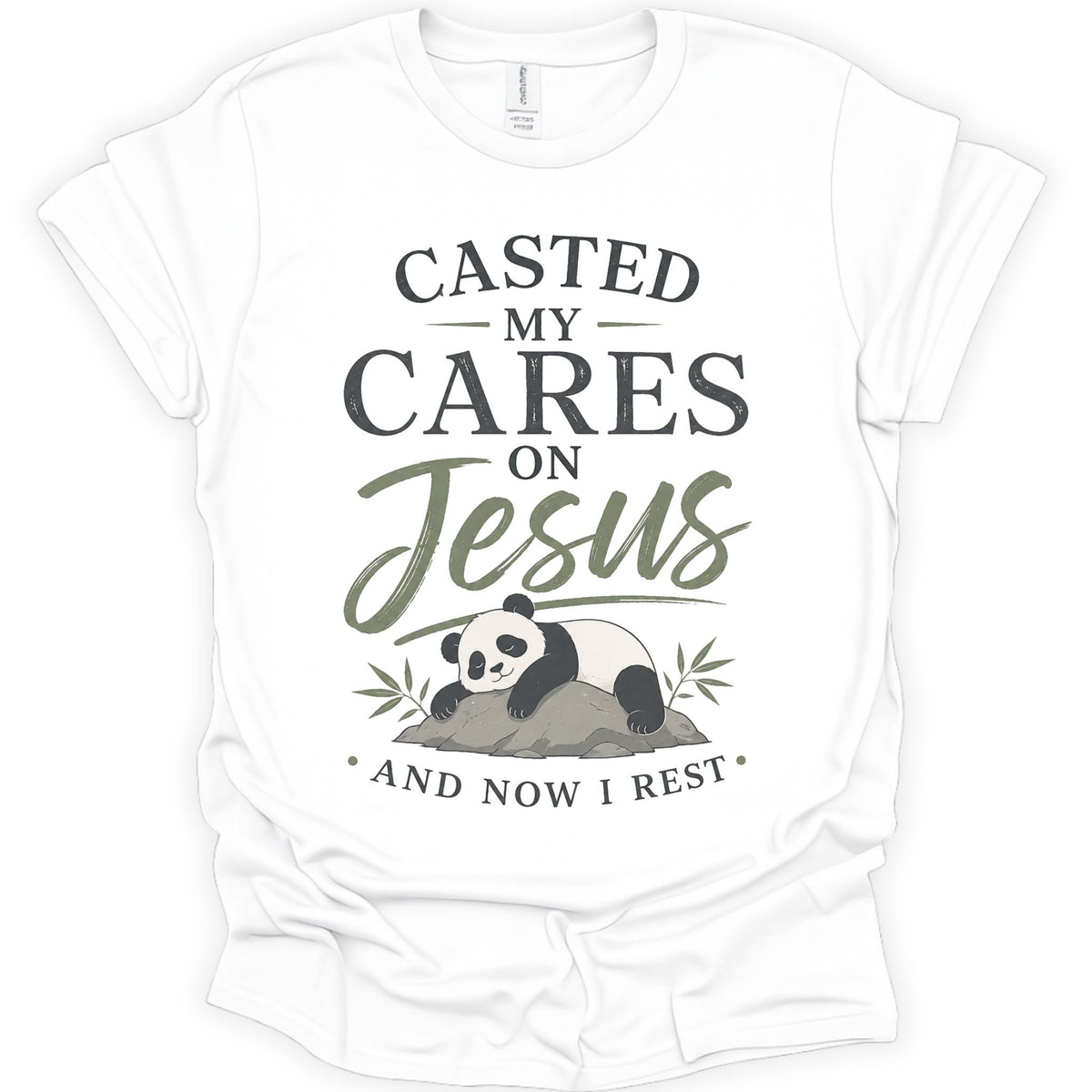 A white short-sleeve crewneck t-shirt with a graphic print on the front. The print features the text 'CASTED MY CARES ON Jesus AND NOW I REST' in dark gray and olive green lettering, accompanied by an illustration of a sleeping panda resting on a rock with bamboo leaves.