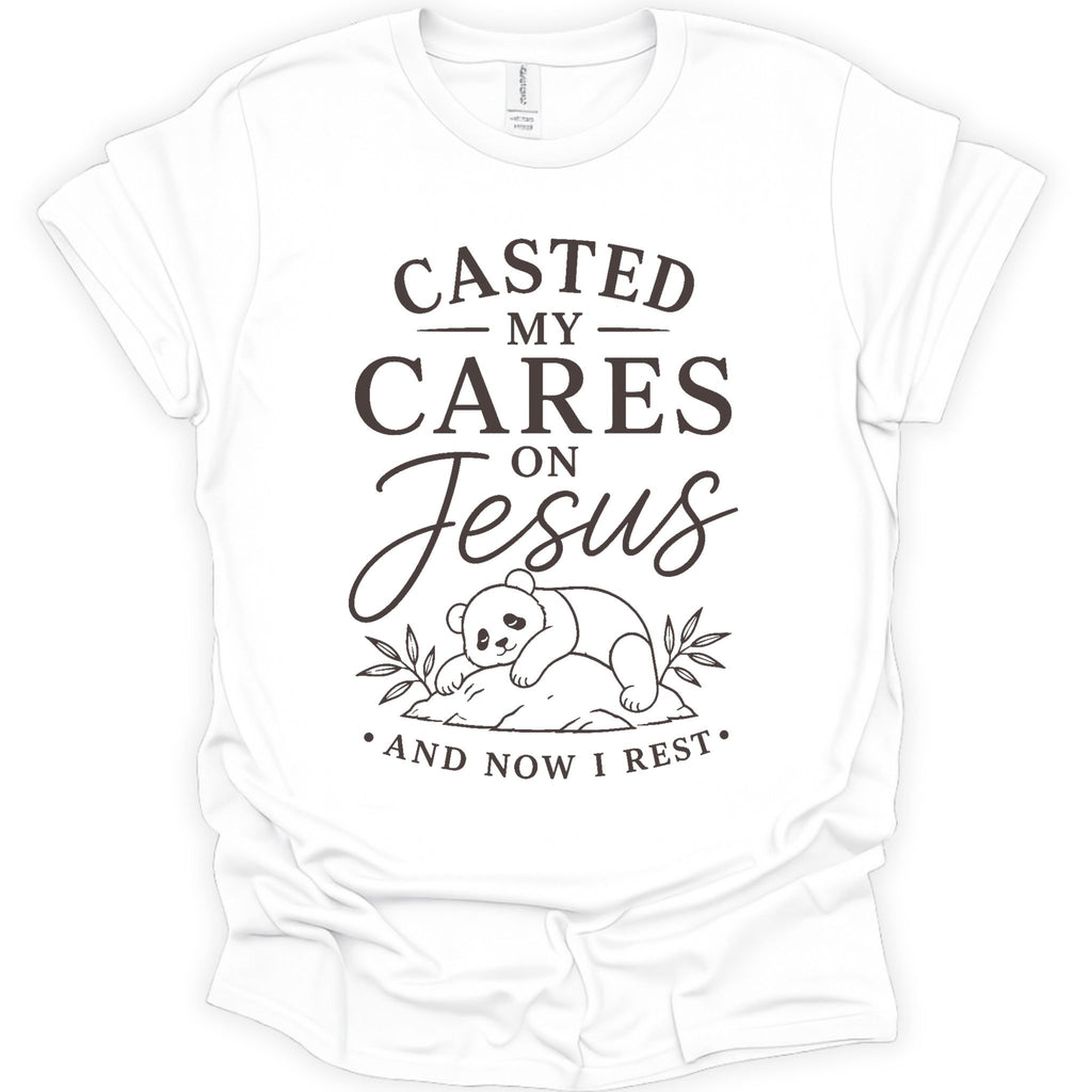 A white short-sleeve crewneck t-shirt with a dark brown graphic print on the front. The graphic features the text 'CASTED MY CARES ON Jesus AND NOW I REST' in a mix of serif and cursive fonts, accompanied by a simple line drawing of a baby panda resting on a rock with leaves.