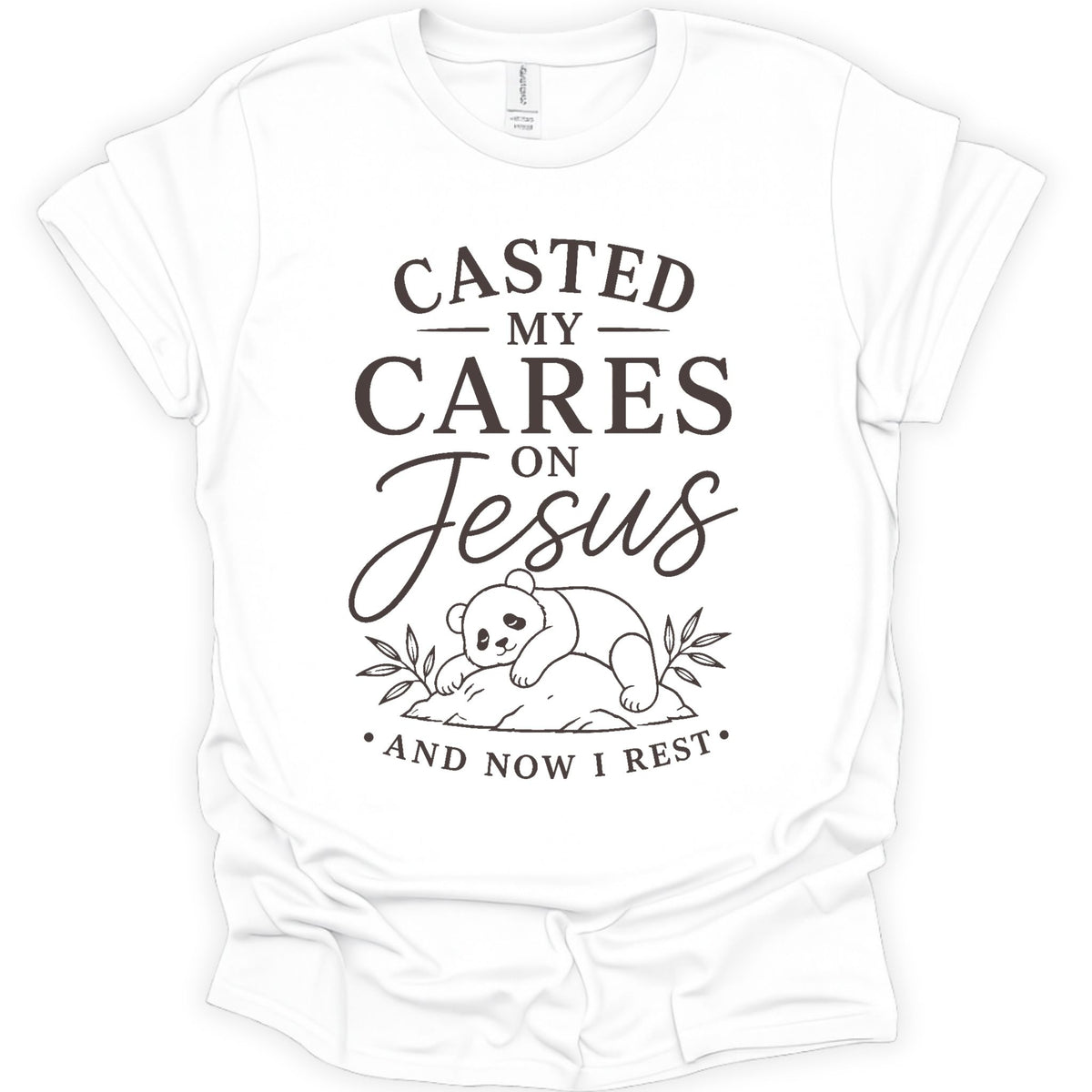 A white short-sleeve crewneck t-shirt with a dark brown graphic print on the front. The graphic features the text 'CASTED MY CARES ON Jesus AND NOW I REST' in a mix of serif and cursive fonts, accompanied by a simple line drawing of a baby panda resting on a rock with leaves.