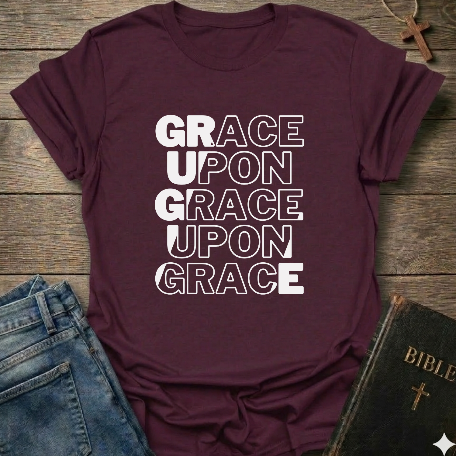 Maroon t-shirt with 'GRACE UPON GRACE' Christian T-Shirt John 1:16 bold faith apparel text on a wooden surface with jeans and a Bible.