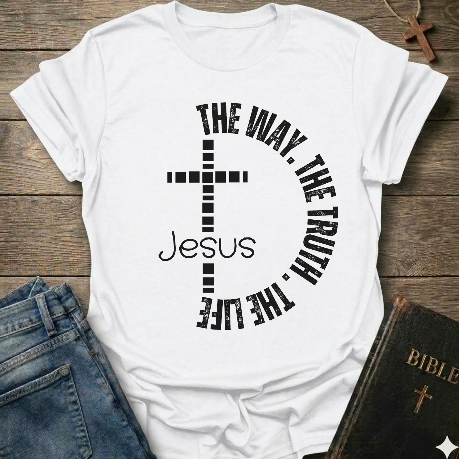 White t-shirt with a cross and text  "Jesus The Way The Truth The Life Cross Circle John 14:6" Christian faith apparel Faith Forward. It is on a wooden surface with jeans and a Bible.