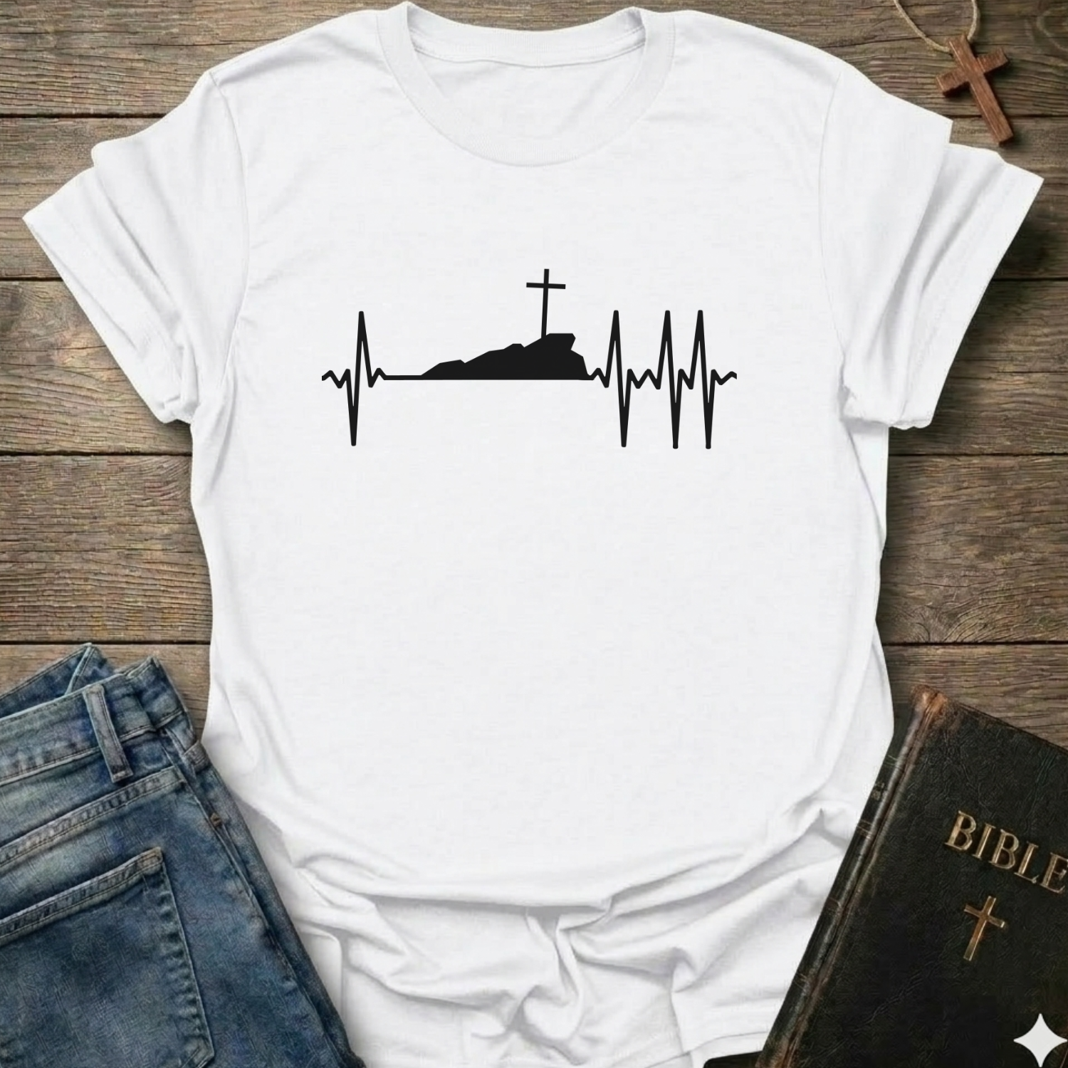 White T-shirt with a white graphic design Cross Heartbeat Lifeline Christian minimal faith apparel conversation starter on a wooden surface with jeans and a Bible.