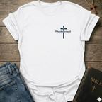 White t-shirt with a cross and 'Redeemed' text Christian minimal faith apparel Faith Forward on a wooden surface with jeans and a Bible.