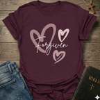 Maroon t-shirt with 'Forgiven' text and pink hearts on a wooden surface with jeans and a Bible. Forgiven Christian T-Shirt 1 John 1:9 bold faith apparel Faith Forward women