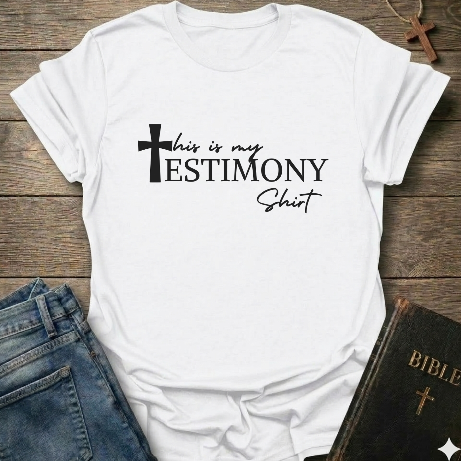 White t-shirt with 'This is my testimony shirt' text and cross minimal faith apparel conversation starter. It is on a wooden surface with jeans and a Bible.