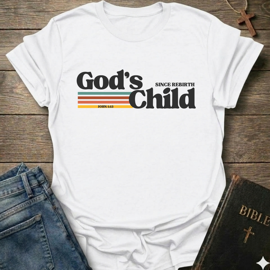 White t-shirt with God's Child Since Rebirth Christian T-Shirt John 1:12 retro faith apparel conversation starter text on a wooden surface with jeans and a Bible.
