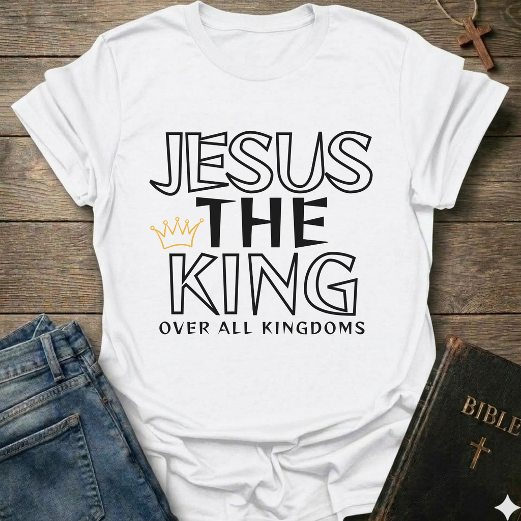 White t-shirt with text 'Jesus The King Over All Kingdoms'  and crown Christian bold faith apparel Faith Forward text on a wooden surface with jeans and a Bible.