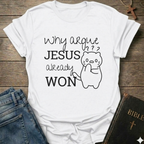A white graphic t-shirt laid flat on a rustic wooden background, styled with blue jeans and a black Bible. The t-shirt features the text 'Why argue JESUS already WON' in black lettering alongside a simple line drawing of a confused cat.