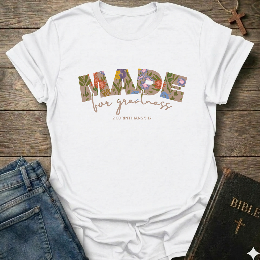White t-shirt with 'Made for greatness' text on a wooden surface with jeans and a Bible. Made for Greatness Christian T-Shirt 2 Corinthians 5:17 bold faith apparel Faith Forward women