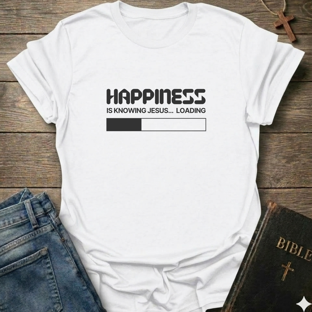 A white short-sleeve graphic T-shirt  laid flat on a rustic wooden surface, styled with blue jeans and a Bible. The t-shirt features a black printed loading bar "like a battery charging" graphic that reads 'HAPPINESS IS KNOWING JESUS.