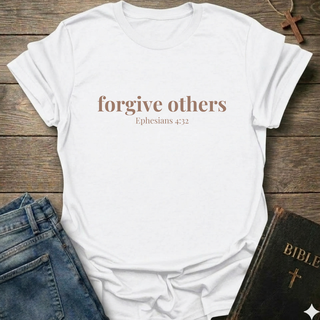 White t-shirt with 'forgive others Ephesians 4:32' text on a wooden surface with jeans and a Bible.