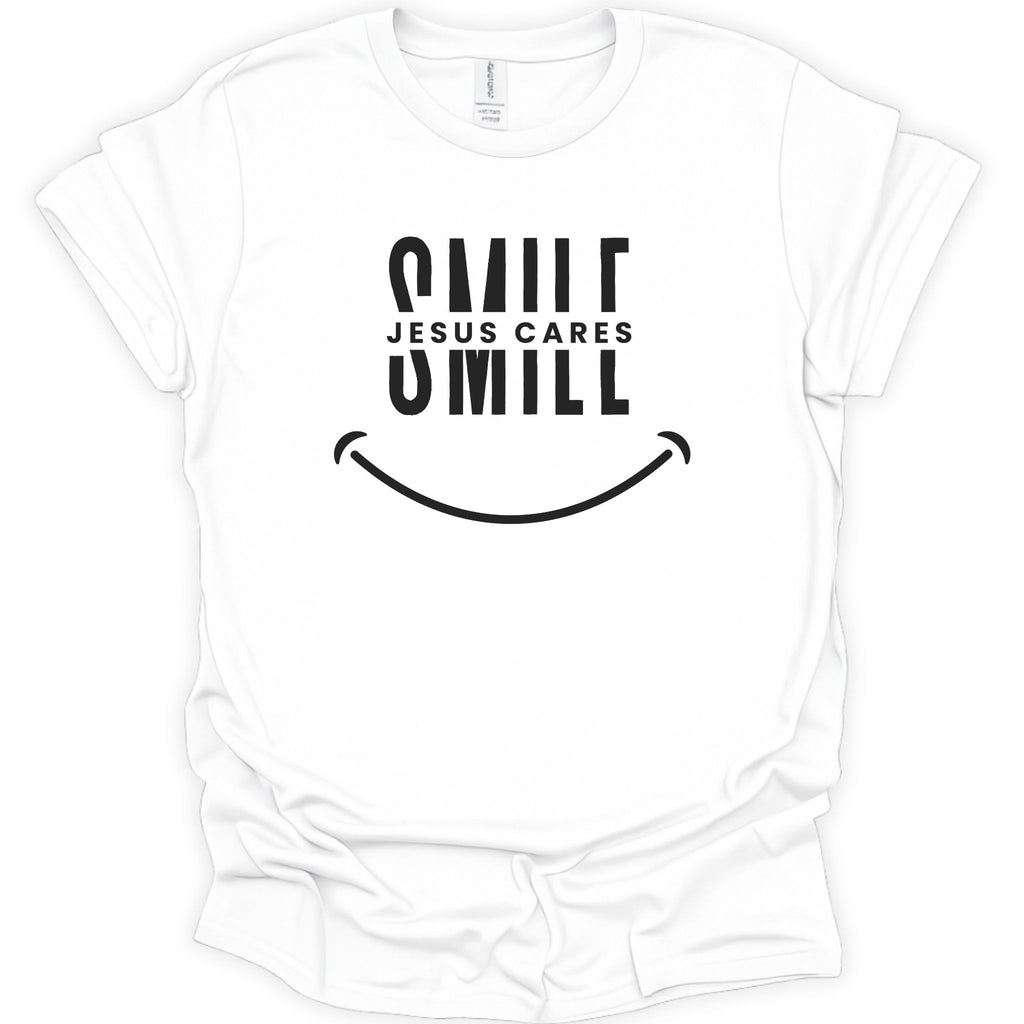 A white short-sleeve crewneck t-shirt with a black graphic print on the front reading 'SMILE JESUS CARES' and a smiley face, shown on a plain white background.