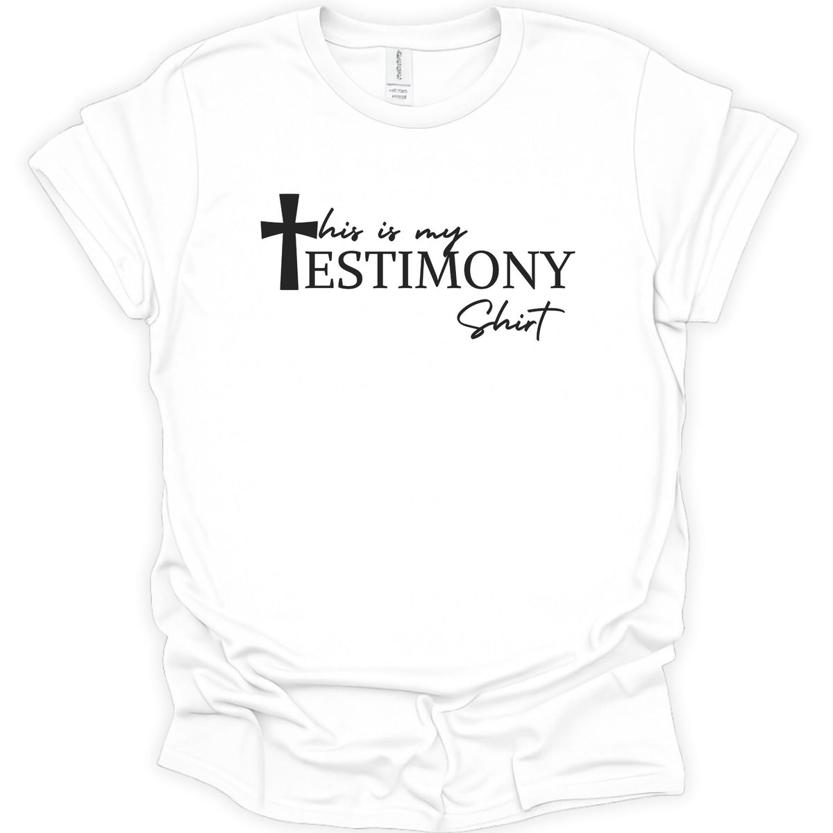 A white short-sleeve crewneck t-shirt with a black graphic text print reading 'this is my TESTIMONY Shirt' accompanied by a cross icon, displayed on a clean white background.