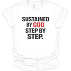 A white short-sleeve crewneck t-shirt with a graphic text print reading 'SUSTAINED BY GOD STEP BY STEP.' in bold black and red lettering, displayed on a clean white background.