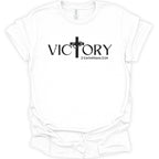 A white short-sleeve crewneck t-shirt with a black graphic on the chest featuring the word 'VICTORY' in a stylized serif font, a cross, and the Bible verse '2 Corinthians 2:14'.