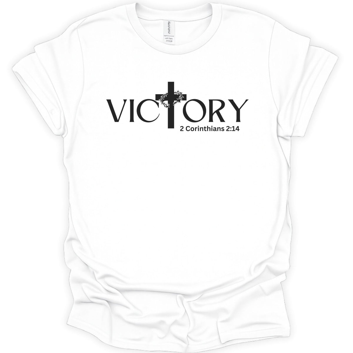 A white short-sleeve crewneck t-shirt with a black graphic on the chest featuring the word 'VICTORY' in a stylized serif font, a cross, and the Bible verse '2 Corinthians 2:14'.