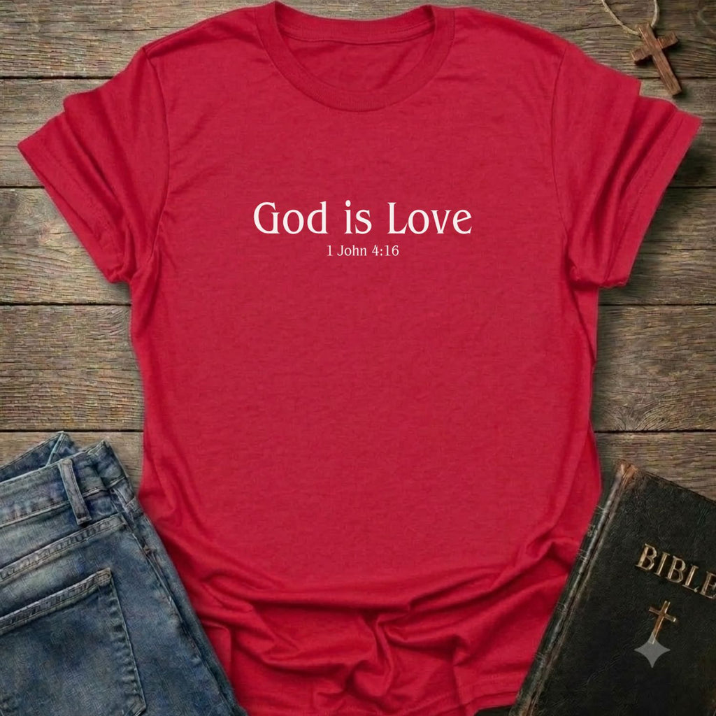 A red short-sleeve crewneck t-shirt with the text 'God is Love 1 John 4:16' printed in white on the chest. The shirt is styled in a flat-lay arrangement on a rustic wooden background, accompanied by blue jeans and a black leather-bound Bible.