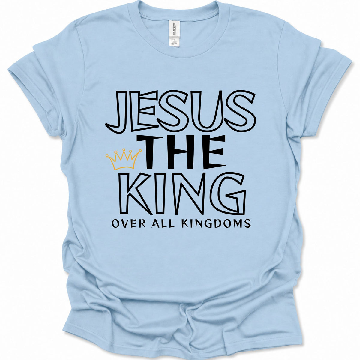 A light blue short-sleeve t-shirt with a graphic print reading 'JESUS THE KING OVER ALL KINGDOMS' in black outlined lettering, accented by a small gold crown icon, displayed on a clean white background.