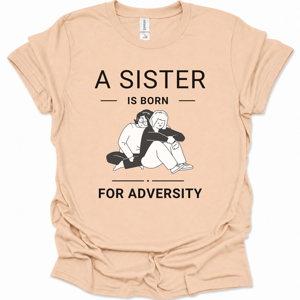 A natural-colored short-sleeve t-shirt with a black graphic print that reads 'A SISTER IS BORN FOR ADVERTS' surrounding an illustration of two people hugging. The shirt is laid flat on a white background.
