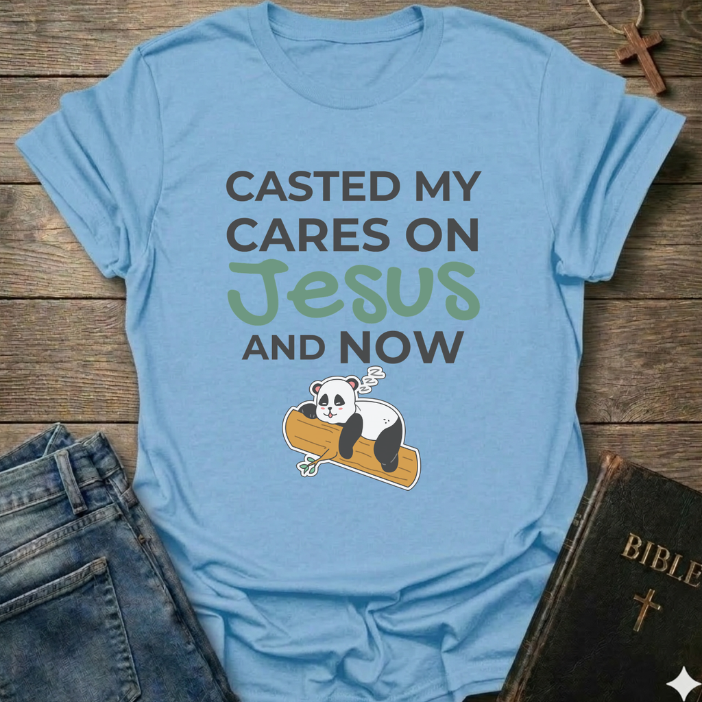 Blue t-shirt Casted My Cares on Jesus Christian relatable faith apparel conversation starter with a panda graphic and text on a wooden surface with jeans and a Bible.