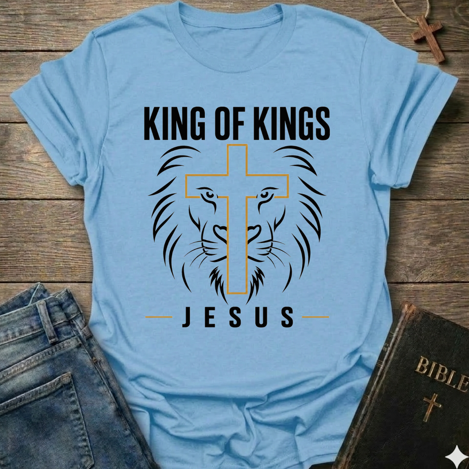 Light blue t-shirt with 'King of Kings Jesus Lion Cross Revelation 19:16 faith apparel conversation starter' on a wooden surface. 
