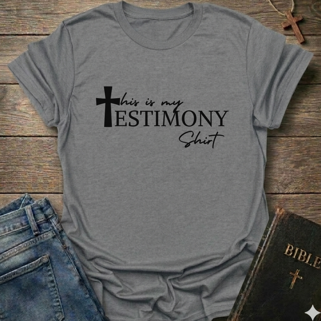 Gray t-shirt with 'This is my testimony shirt' text and cross minimal faith apparel conversation starter. It is on a wooden surface with jeans and a Bible.