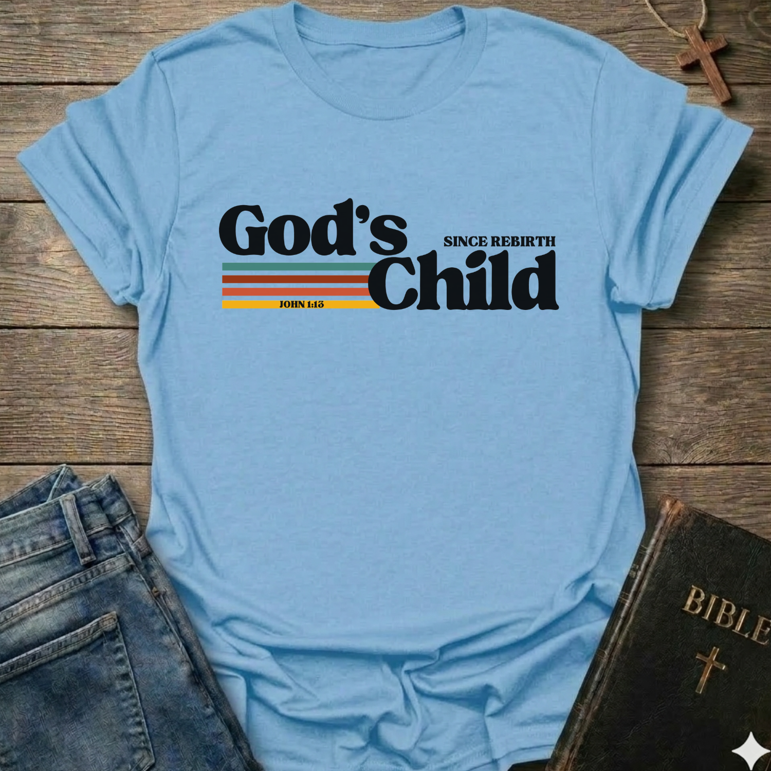 Light blue t-shirt with God's Child Since Rebirth Christian T-Shirt John 1:12 retro faith apparel conversation starter text on a wooden surface with jeans and a Bible.