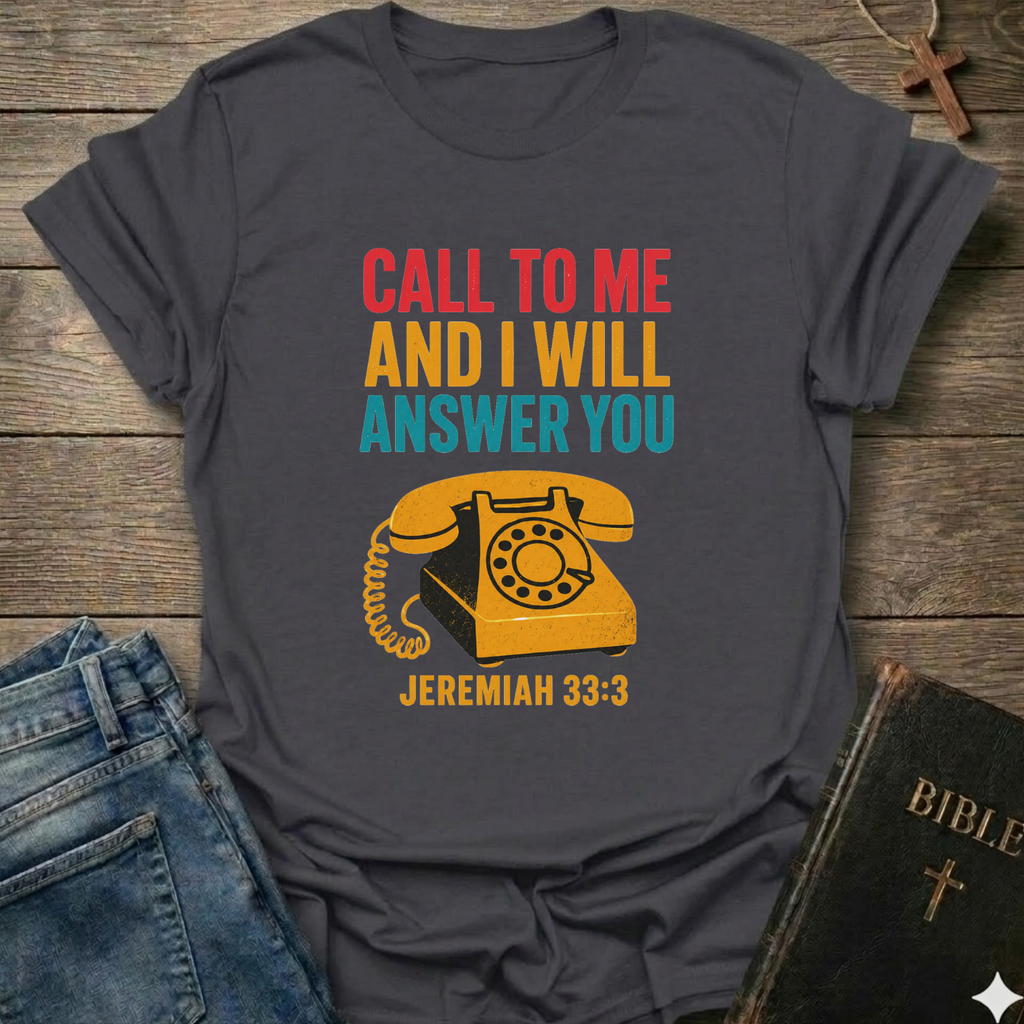 Gray t-shirt with vintage phone graphic and text Call to Me and I Will Answer You Jeremiah 33:3 retro phone faith Christian apparel conversation starter on a wooden surface with jeans and a Bible.