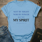 Light blue Christian T-Shirt with text Not by Might but by My Spirit  Zechariah 4:6 faith apparel conversation starter inspirational quote on a wooden surface with jeans and a Bible.