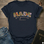 Navy blue t-shirt with 'Made for greatness' text on a wooden surface with jeans and a Bible.