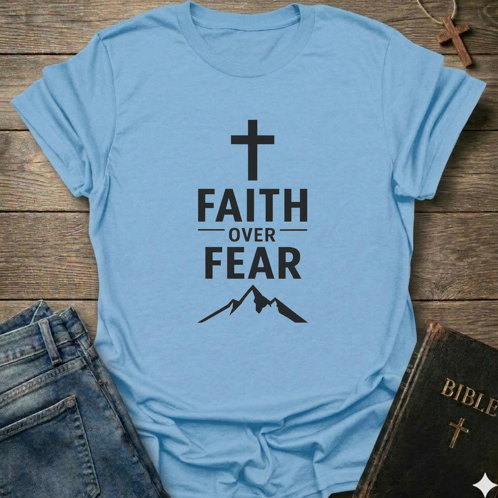 Light blue t-shirt with 'Faith Over Fear' Cross Mountain Christian faith apparel conversation starter design on a wooden surface with jeans and a Bible.