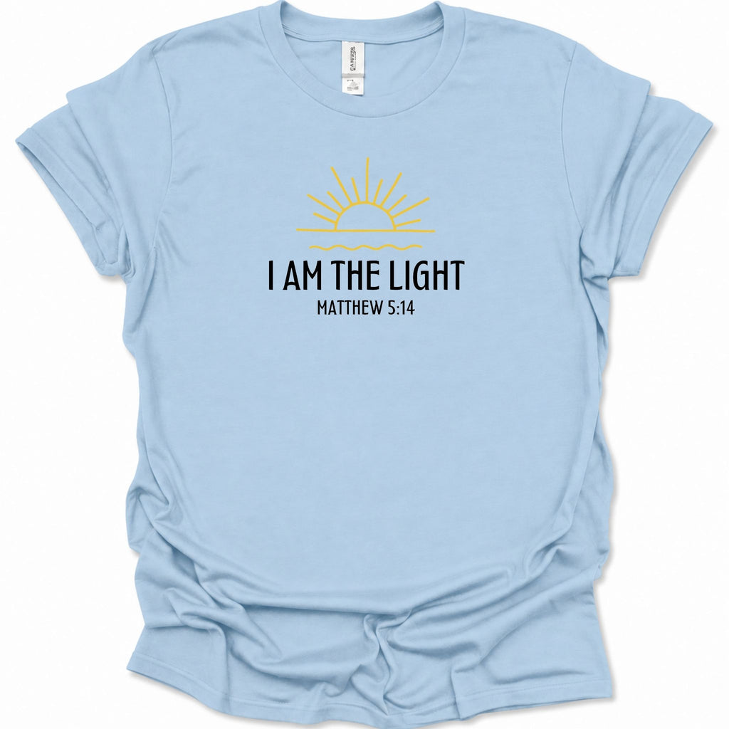 A light blue short-sleeve t-shirt with a graphic on the chest featuring a yellow sun and the text 'I AM THE LIGHT MATTHEW 5:14' in black. The shirt is displayed flat against a clean white background.