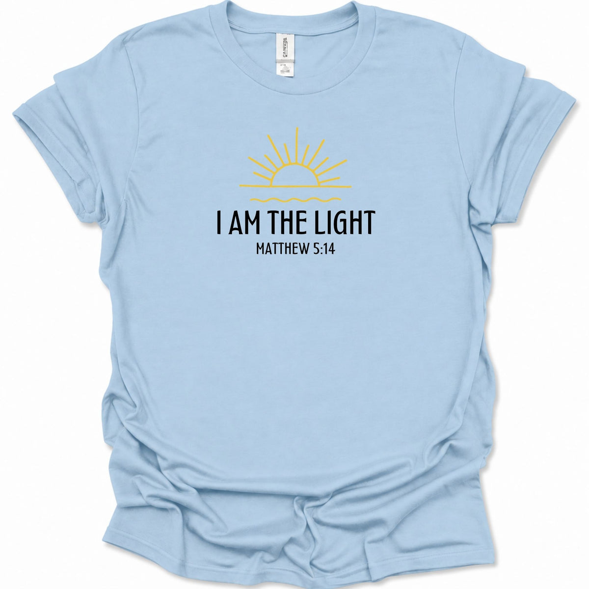 A light blue short-sleeve t-shirt with a graphic on the chest featuring a yellow sun and the text 'I AM THE LIGHT MATTHEW 5:14' in black. The shirt is displayed flat against a clean white background.