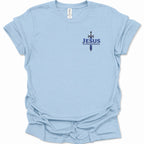 A light blue short-sleeve t-shirt with a small graphic on the left chest featuring a sword and the text  'JESUS ALPHA & OMEGA' in dark blue. The shirt is shown flat against a white background.