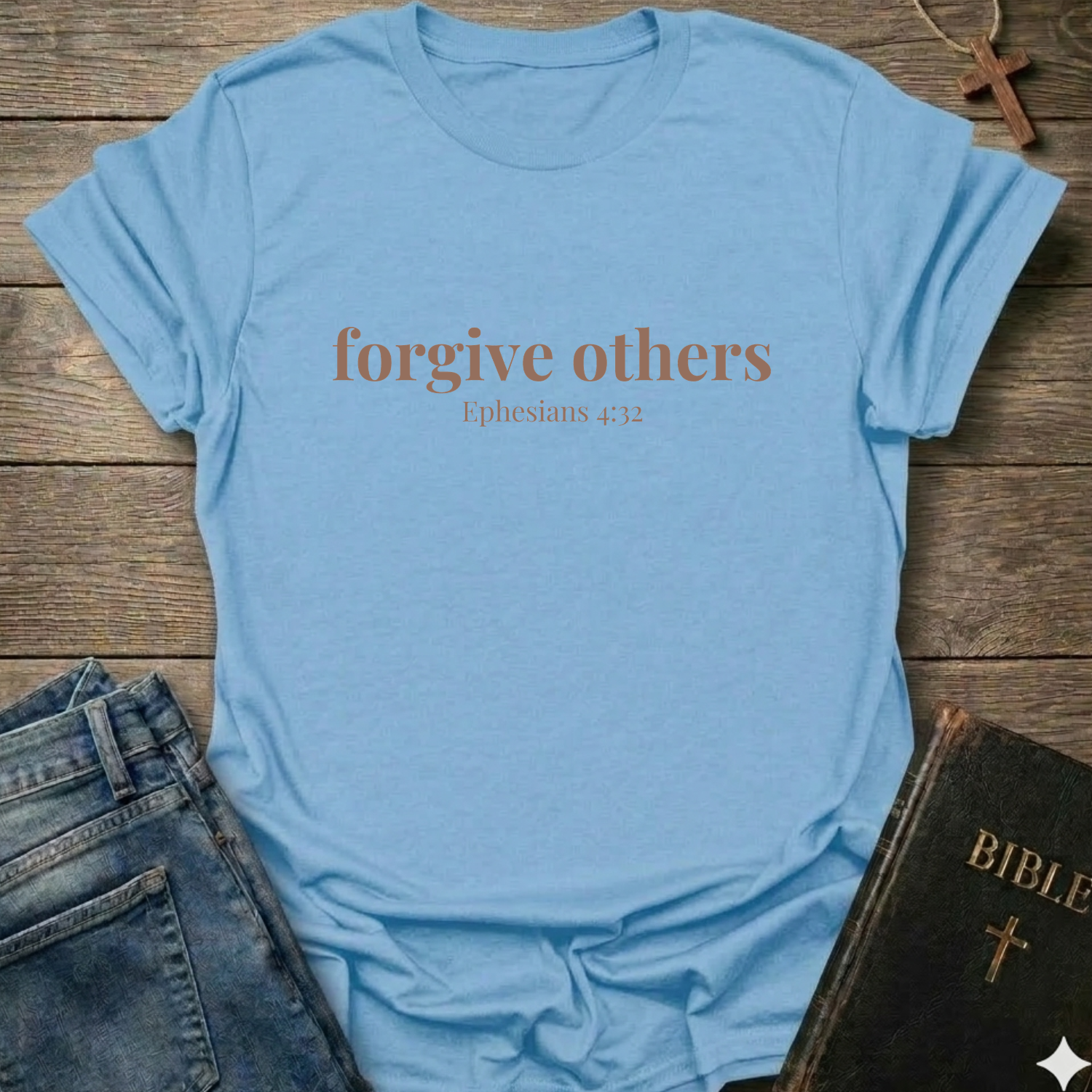 Light blue t-shirt with 'forgive others Ephesians 4:32' text on a wooden surface with jeans and a Bible.