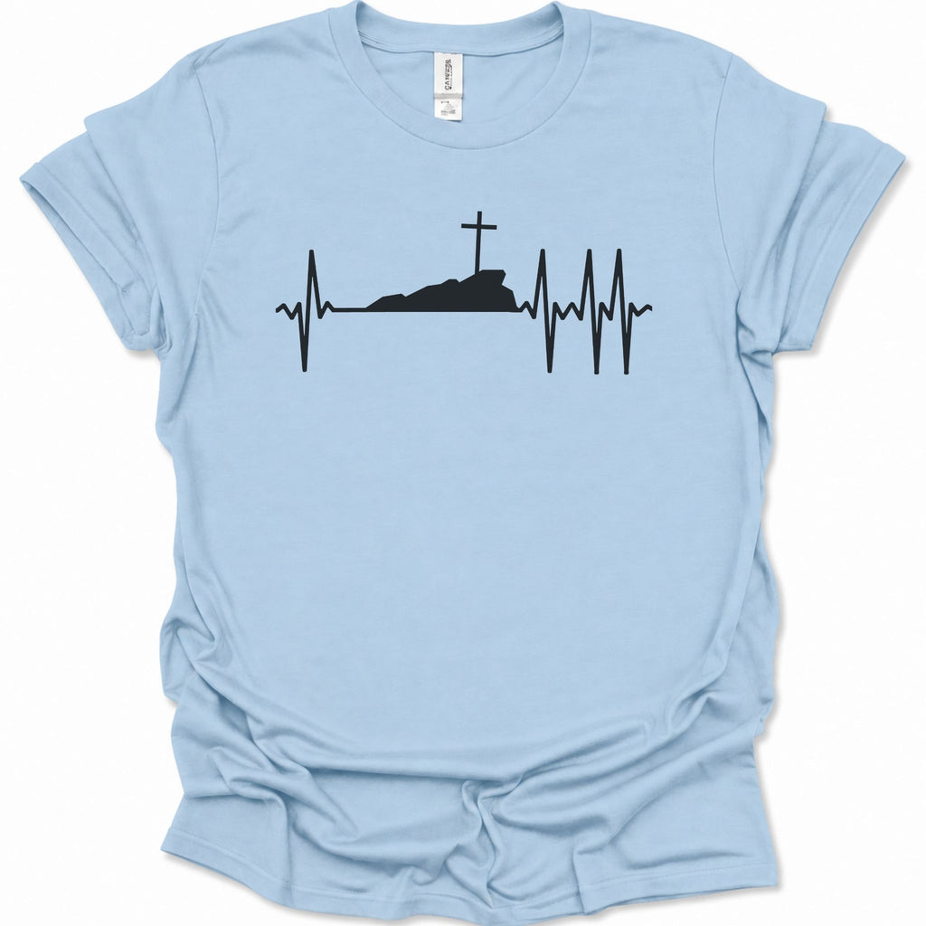 A light blue short-sleeve t-shirt with a black graphic of a heartbeat EKG line forming a cross on a hill, displayed flat against a white background.