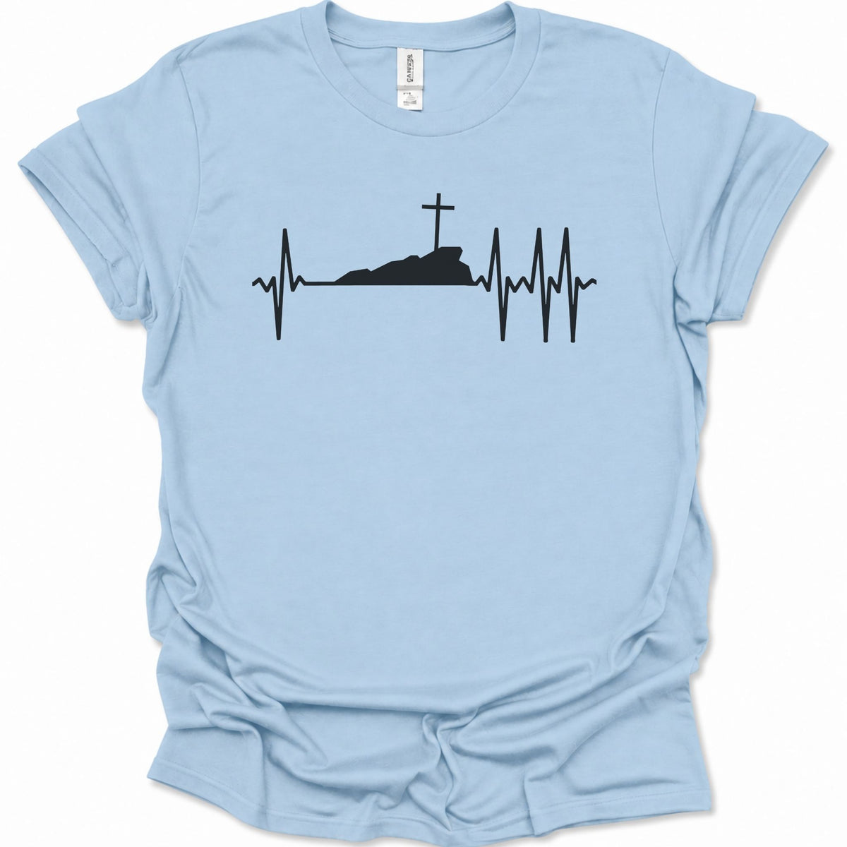 A light blue short-sleeve t-shirt with a black graphic of a heartbeat EKG line forming a cross on a hill, displayed flat against a white background.