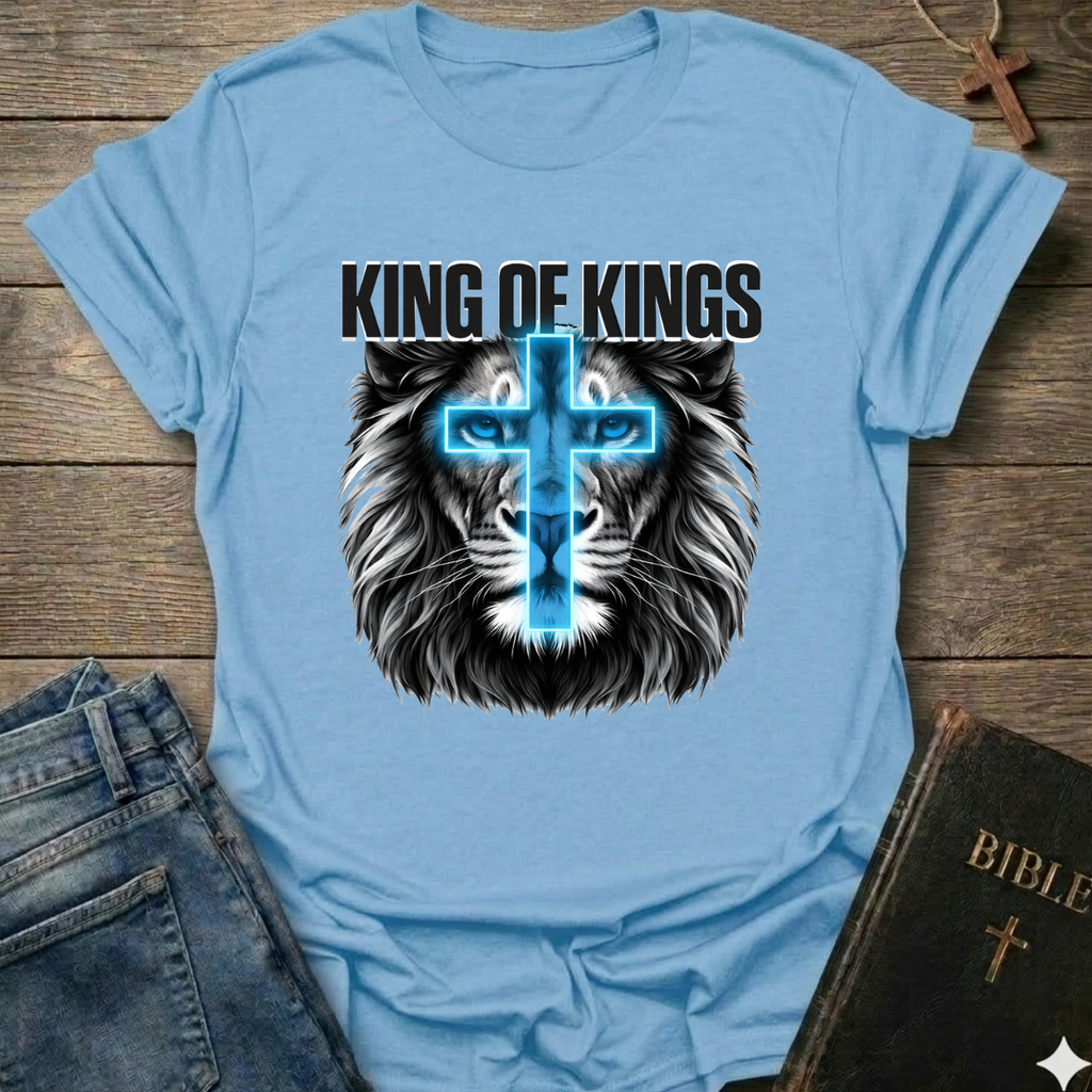 Light blue Christian T-Shirt with lion graphic and 'King of Kings' text Revelation 19:16 bold faith apparel conversation starter on a wooden surface with jeans and a Bible.