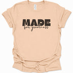 A light natural-colored short-sleeve t-shirt with 'MADE for greatness' printed in black across the chest, displayed flat against a white background.