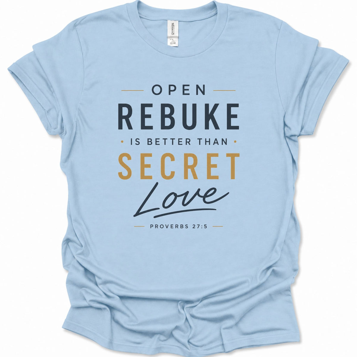 A light blue short-sleeve t-shirt with a printed text graphic on the front reading 'OPEN REBUKE IS BETTER THAN SECRET Love PROVERBS 27:5' in dark gray and mustard yellow lettering, shown on a plain white background.
