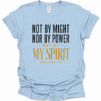 A light blue short-sleeve t-shirt with a printed text graphic on the front reading 'NOT BY MIGHT NOR BY POWER BUT BY MY SPIRIT ZECHARIAH 4:6' in black and gold lettering, displayed on a clean white background.