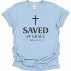 A light blue short-sleeve crewneck t-shirt with a distressed black graphic print on the front featuring a cross, the text 'SAVED BY GRACE', and 'Ephesians 2:8'.