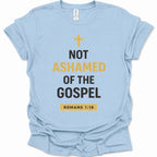 A light blue short-sleeve t-shirt with a graphic print on the front. The print features a yellow cross, the text 'NOT ASHAMED OF THE GOSPEL' in black and yellow, and 'ROMANS 1:16' inside a yellow box at the bottom.