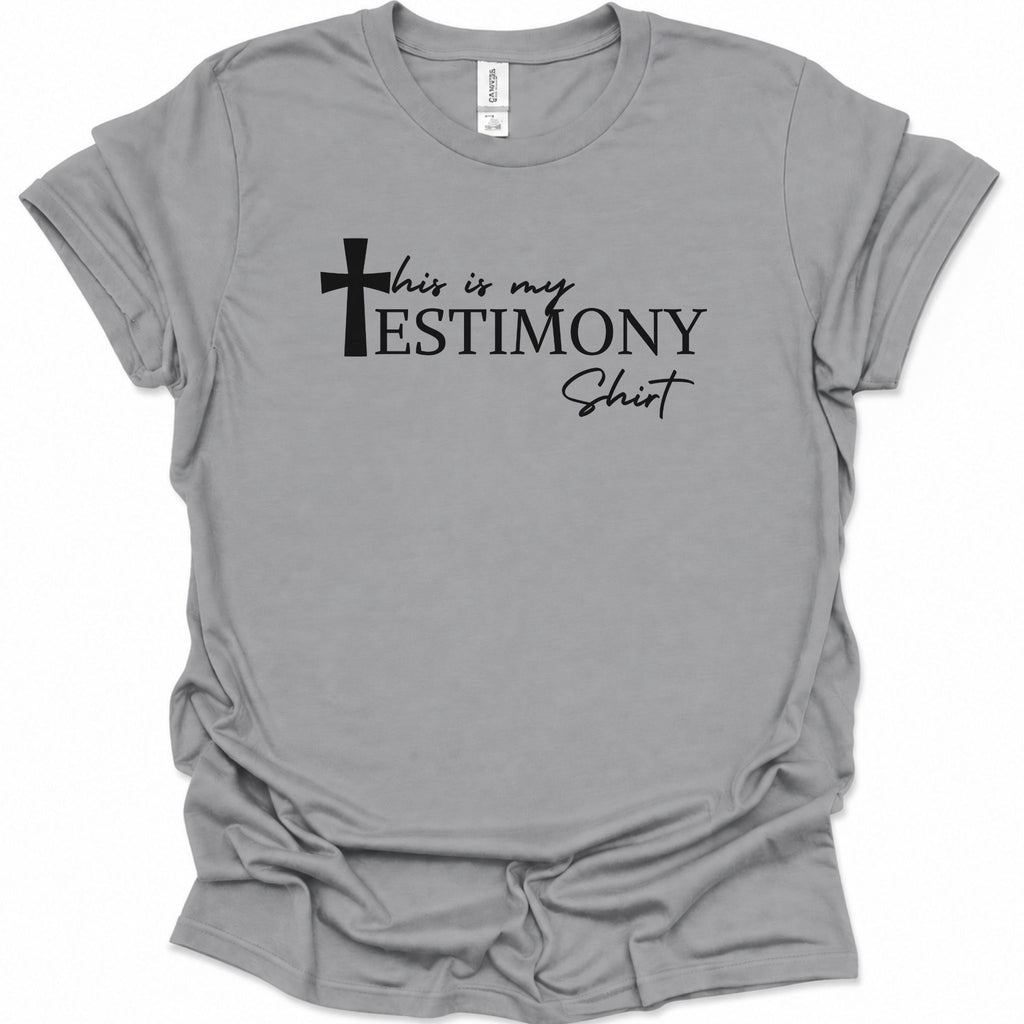 A sport gray short-sleeve t-shirt with a black graphic text print reading 'this is my TESTIMONY Shirt' accompanied by a cross icon, displayed on a clean white background.