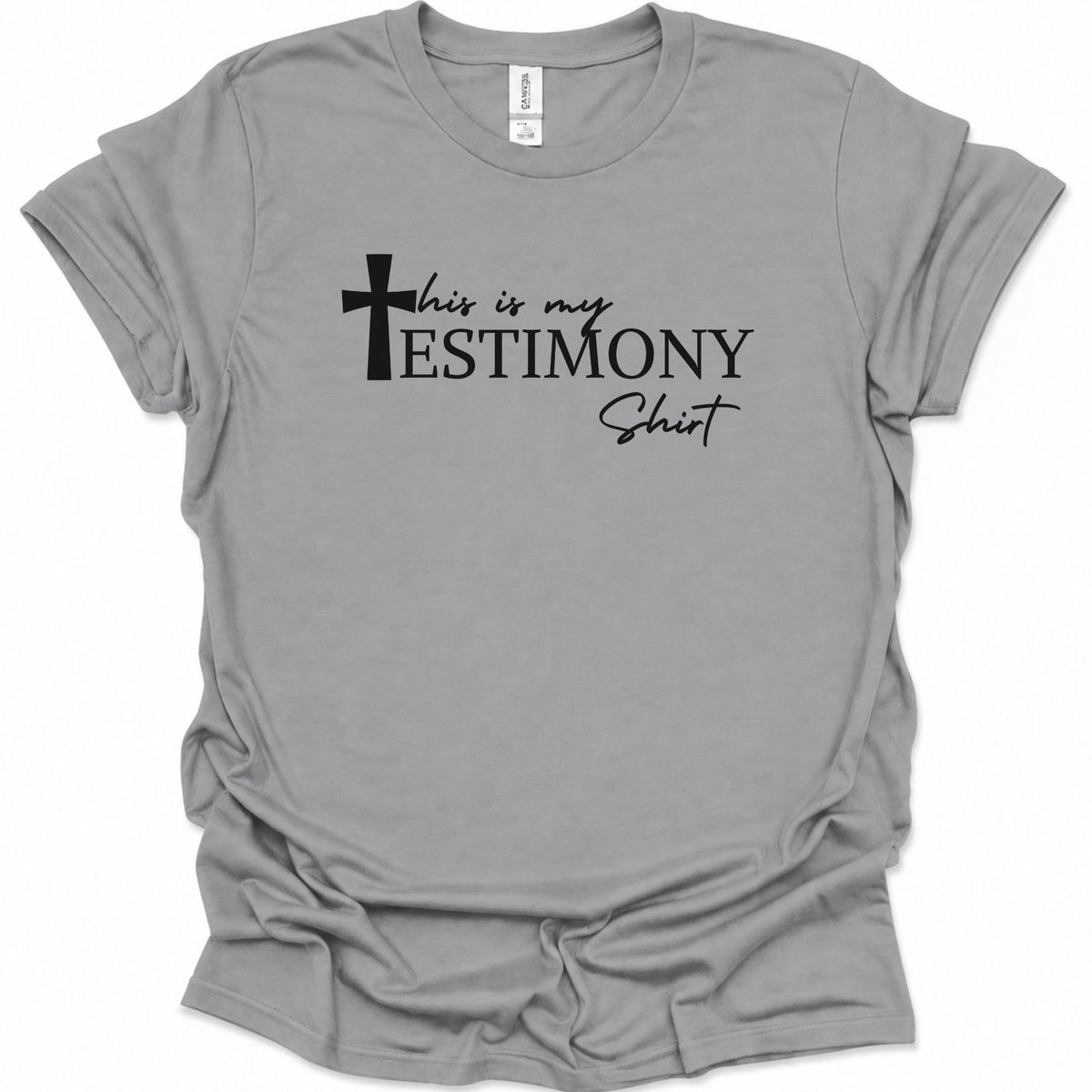 A sport gray short-sleeve t-shirt with a black graphic text print reading 'this is my TESTIMONY Shirt' accompanied by a cross icon, displayed on a clean white background.