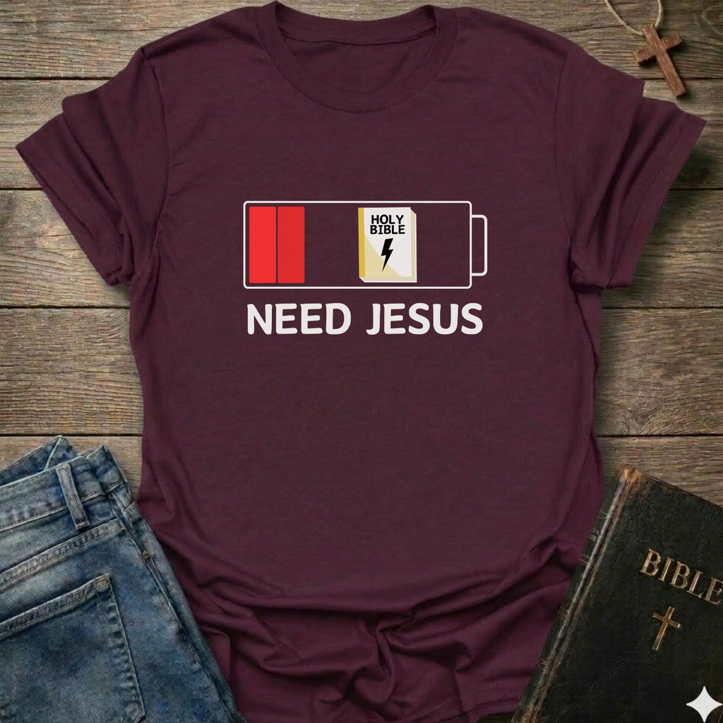 Maroon t-shirt with 'Need Jesus' graphic on a wooden surface with jeans and a Bible. Need Jesus to Recharge My Battery Christian T-Shirt bold faith apparel Faith Forward
