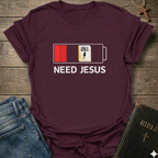 Maroon t-shirt with 'Need Jesus' graphic on a wooden surface with jeans and a Bible. Need Jesus to Recharge My Battery Christian T-Shirt bold faith apparel Faith Forward