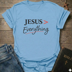 Light blue T-Shirt faith apparel conversation starter with 'JESUS > Everything' text on a wooden surface with jeans and a Bible.