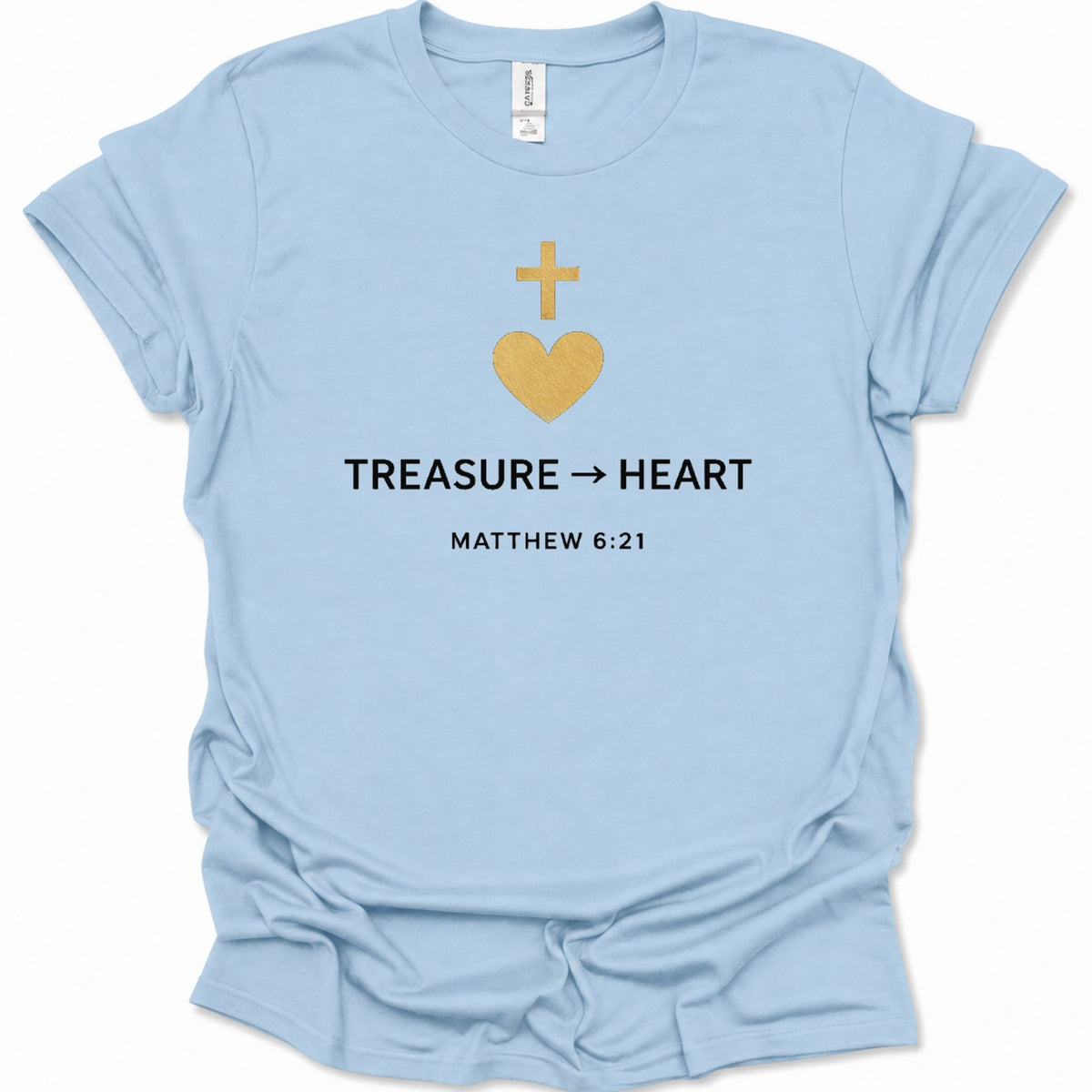 A light blue short-sleeve t-shirt with a graphic on the chest featuring a gold heart and cross, the text 'TREASURE -> HEART', and 'MATTHEW 6:21' in black. The shirt is shown flat against a white background.